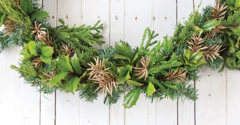 Christmas garland swag made from Southern Living plants greenery, oranges and pine cones set atop a white-washed pallet