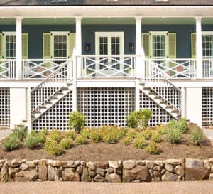 Southern Living Idea House with green siding and white balcony rock walled garden bed in front