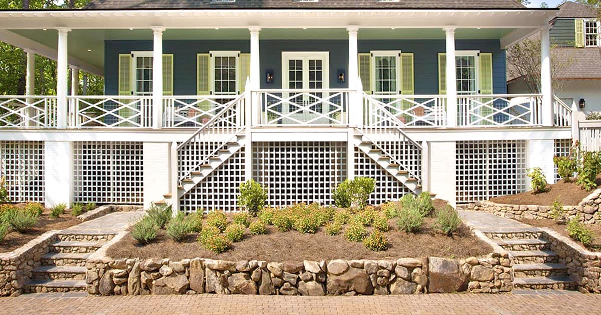 Southern Living Idea House with green siding and white balcony rock walled garden bed in front