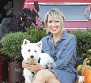 Linda Vater sits with her white Westie dog in the back of a red retro pick-up truck surrounded by Southern Living plant, Pancake Arborvitae