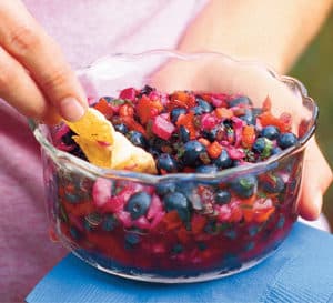 woman holding clear glass bowl of blueberry salsa