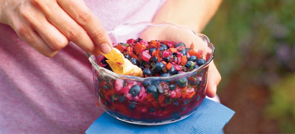 woman holding clear glass bowl of blueberry salsa
