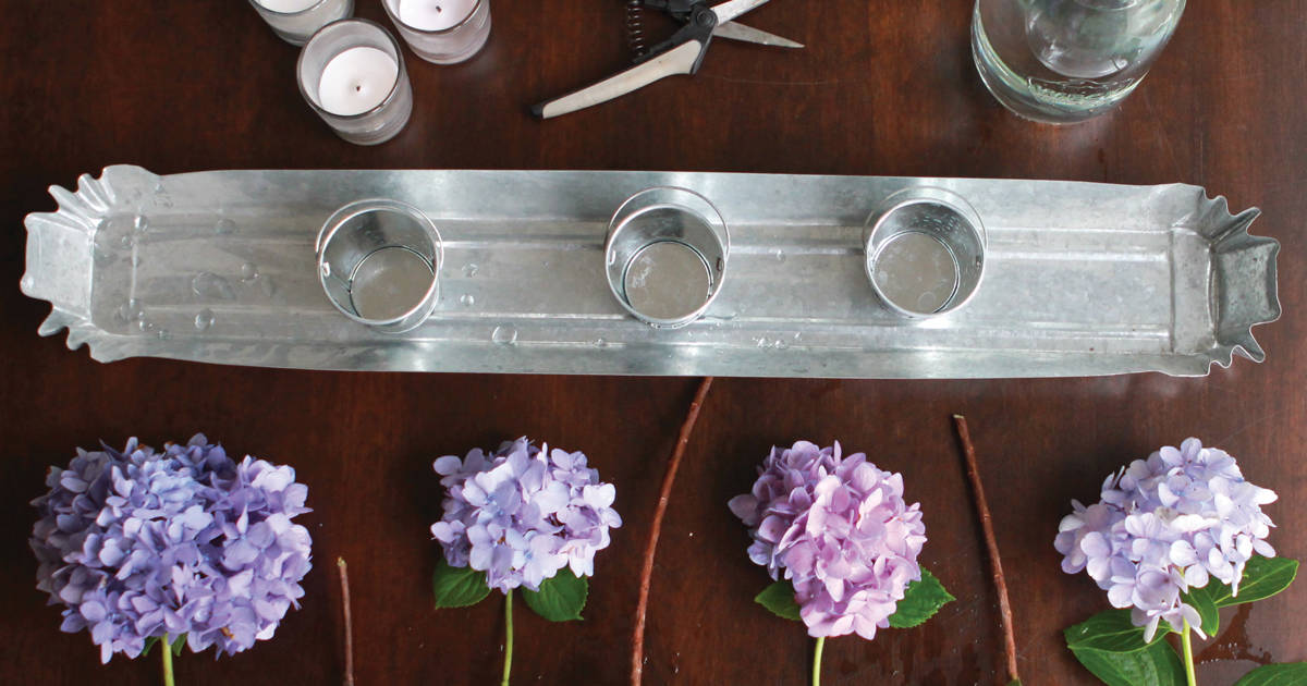 Wooden table with silver runner, silver candle holders and cut Dear Dolores Hydrangea blooms
