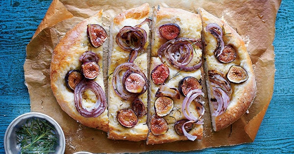 Fig Foccacia with sliced and set atop parchment on a blue table