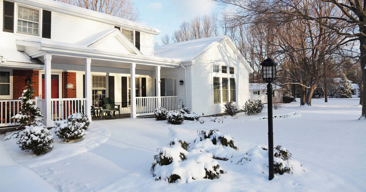 White slat home with black shutters and black lamp post in a snow-covered winter landscape