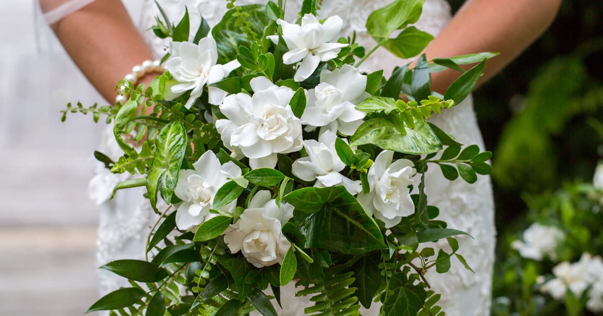 Woman in bridal wear and pearl bracelets holding Gardenia and fern bouquet