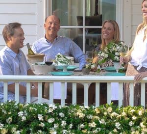 Two couples enjoy a porch dinner surrounded by Jubilation Gardenia blossoms along a white railing