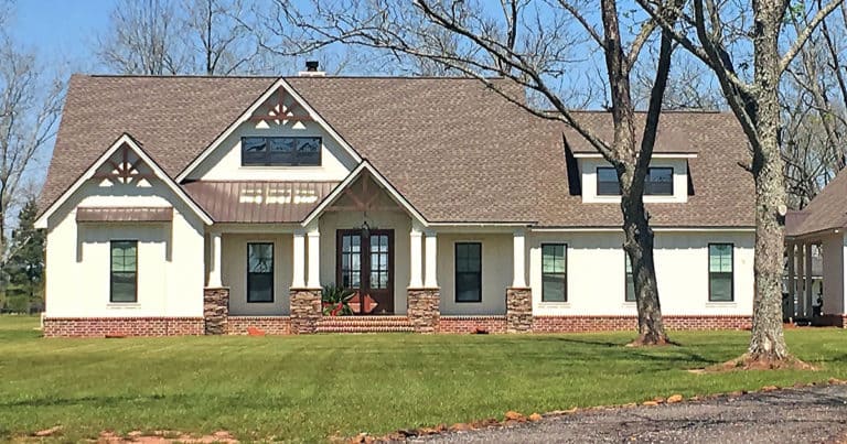 Newly built home with brick and white siding facade and gray shingled roof sits on a newly planted lawn but no landscape plants