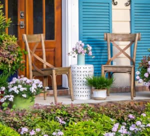 A Southern home facade features extra tall windows & bright blue shutters facing a patio garden full of Southern Living plants