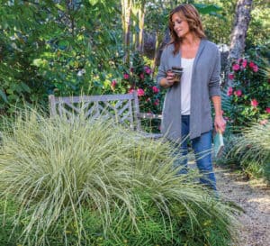 Woman holding book and coffee mug lovingly admiring her garden of Southern Living plants