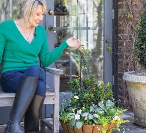 Linda Vater in green shirt, jeans and knee high garden boots sits on porch bench