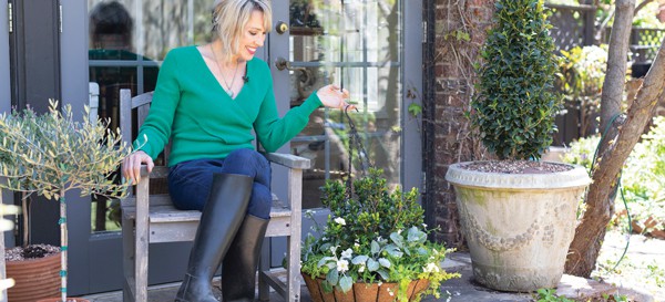 Linda Vater in green shirt, jeans and knee high garden boots sits on porch bench