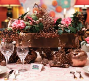 Thanksgiving copper container holding pink roses with cream dinnerware and white lit candles