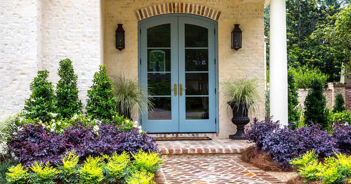 Brick patio with blue door framed with symmetrical planting of Southern Living plants in the garden and in container