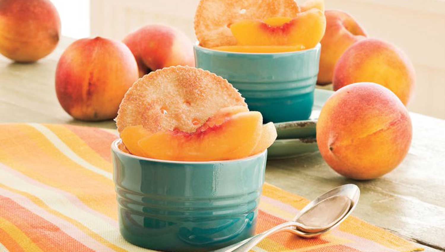 Whole, ripe, red-orange to yellow peaches and blue custard dishes full of a peach dessert