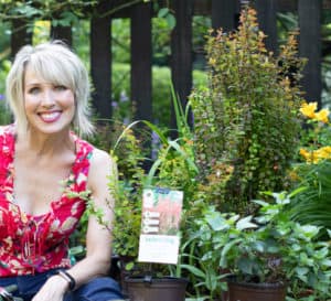 Linda Vater in a red blouse posing with newly arrived Southern Living plants before she plants them in her garden