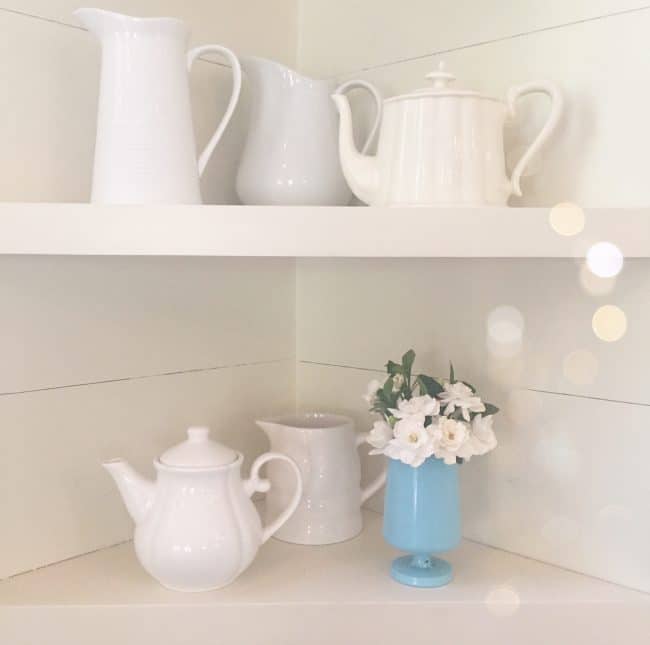 White corner shelves arranged with white teapots and a single blue vase full of Jubilation Gardenias